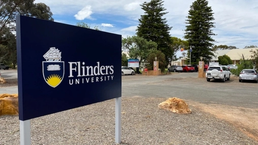 Flinders University outdoor campus sign on a post in a car park with trees and buildings in the background