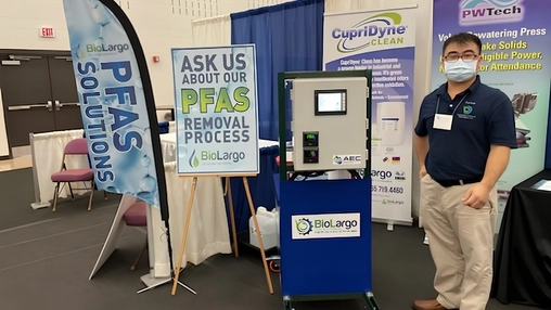 Trade show exhibitor stands beside a BioLargo PFAS removal system and informational displays